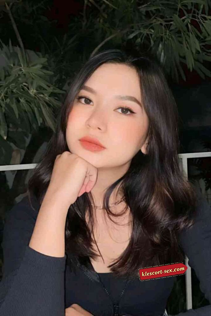 Portrait of a young woman with dark hair, wearing black top, posing with hand on chin.