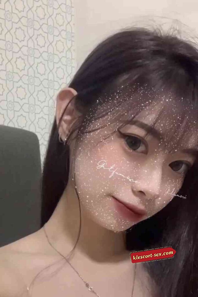 Close-up of a young woman with dark hair, wearing makeup and a glitter filter on her face.