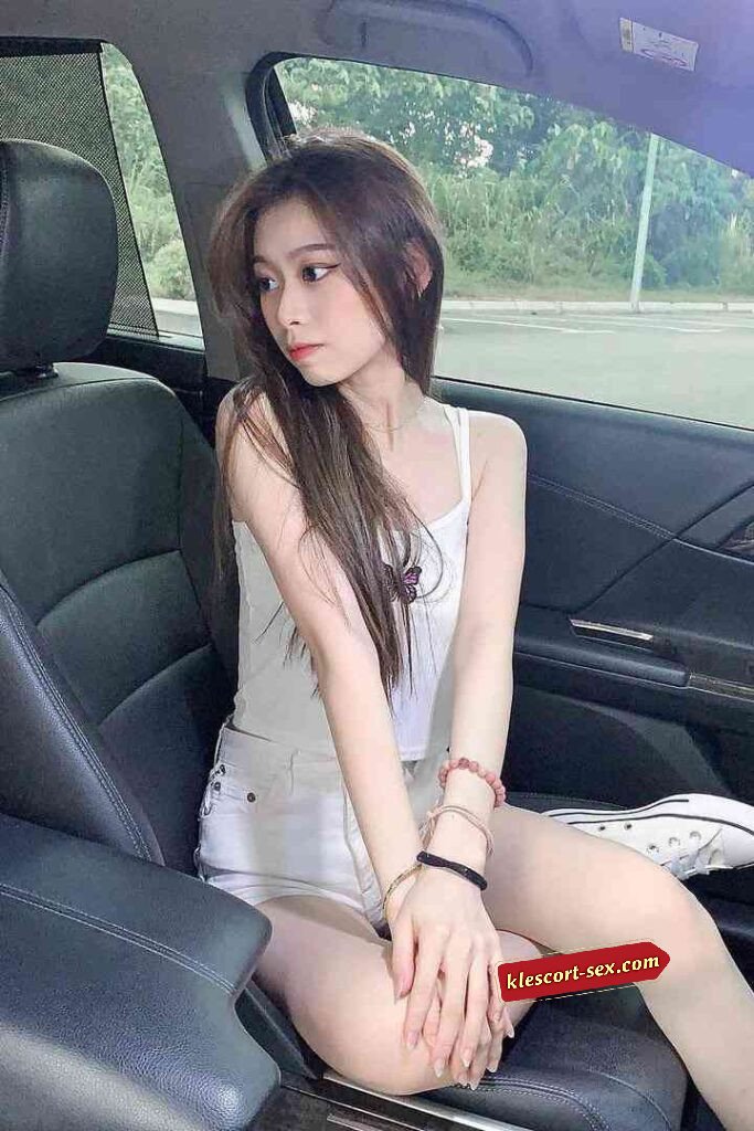 Young woman in car, wearing white top and shorts, looking away.