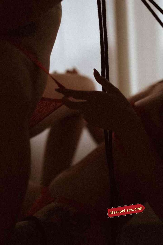 KL Escort Girl Close-up of a person's hand adjusting red lingerie in soft, dim lighting. Sex Service Malaysia