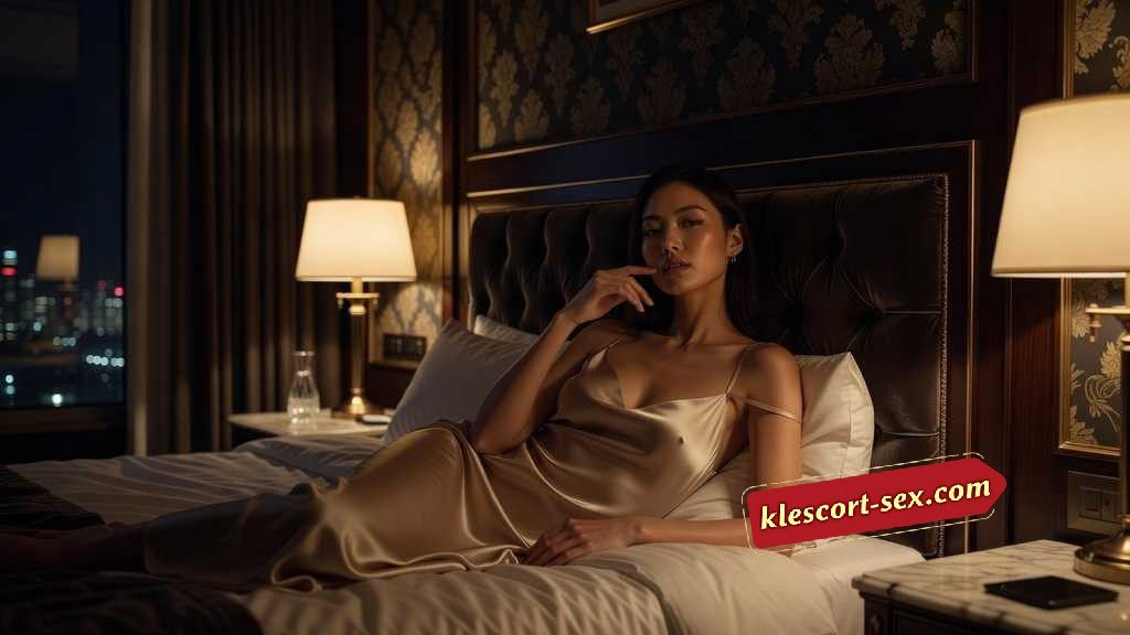 KL Escort Girl Woman in silk slip dress relaxing on a bed in a luxurious hotel room at night. Sex Service Malaysia
