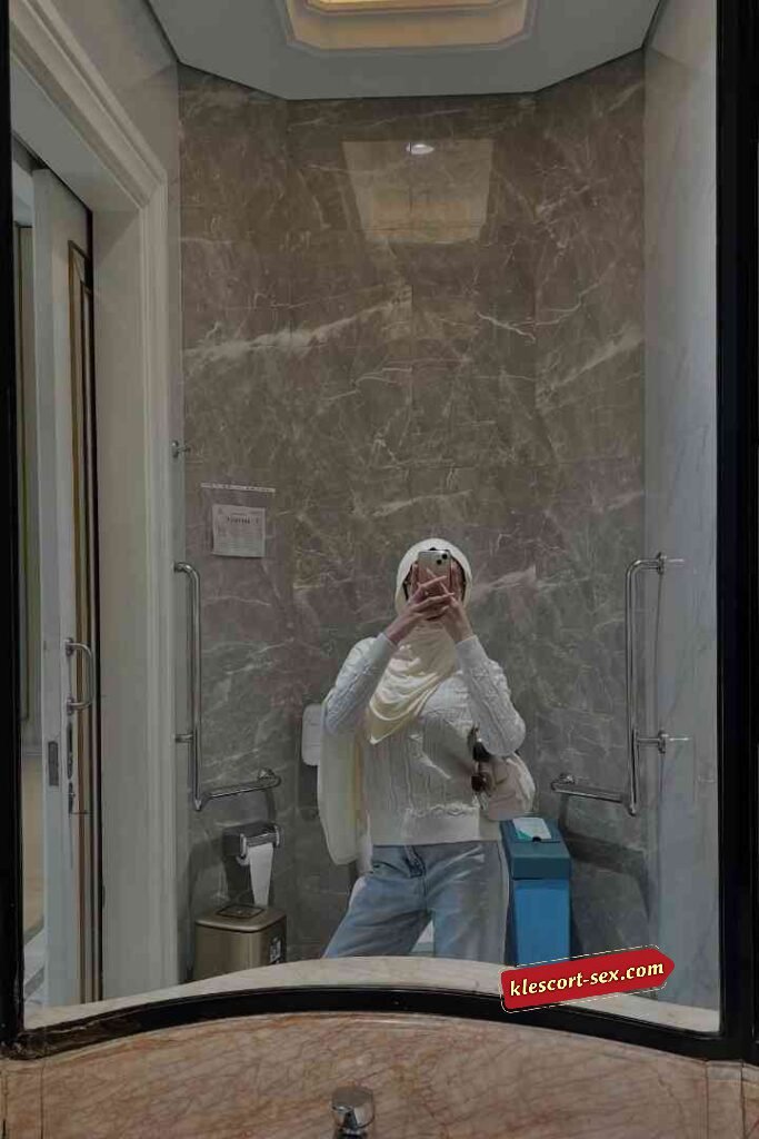 KL Escort Girl Woman in white hijab and sweater takes mirror selfie in marble-tiled bathroom Sex Service Malaysia